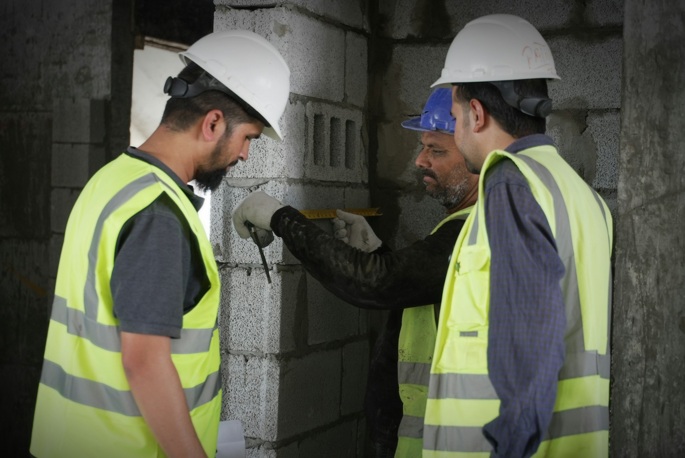 Construction crew in hard hats measuring a concrete block wall